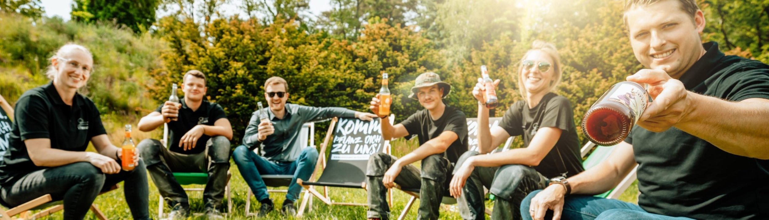Steinhake-Team in den bekannten "Komm, pflanz dich zu uns"-Klappstühlen. Sie sitzen in der Sonne und trinken Limo.
